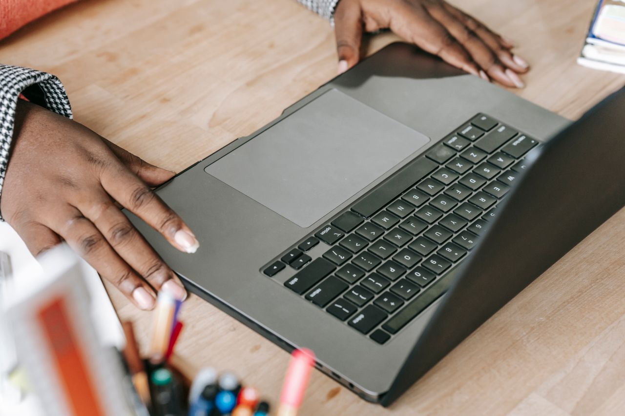 Vue plongeante d’une femme afro-américaine anonyme et occupée, travaillant sur un projet en ligne sur un ordinateur portable posé sur une table